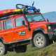 An orange Land Rover Defender parked on a hill.